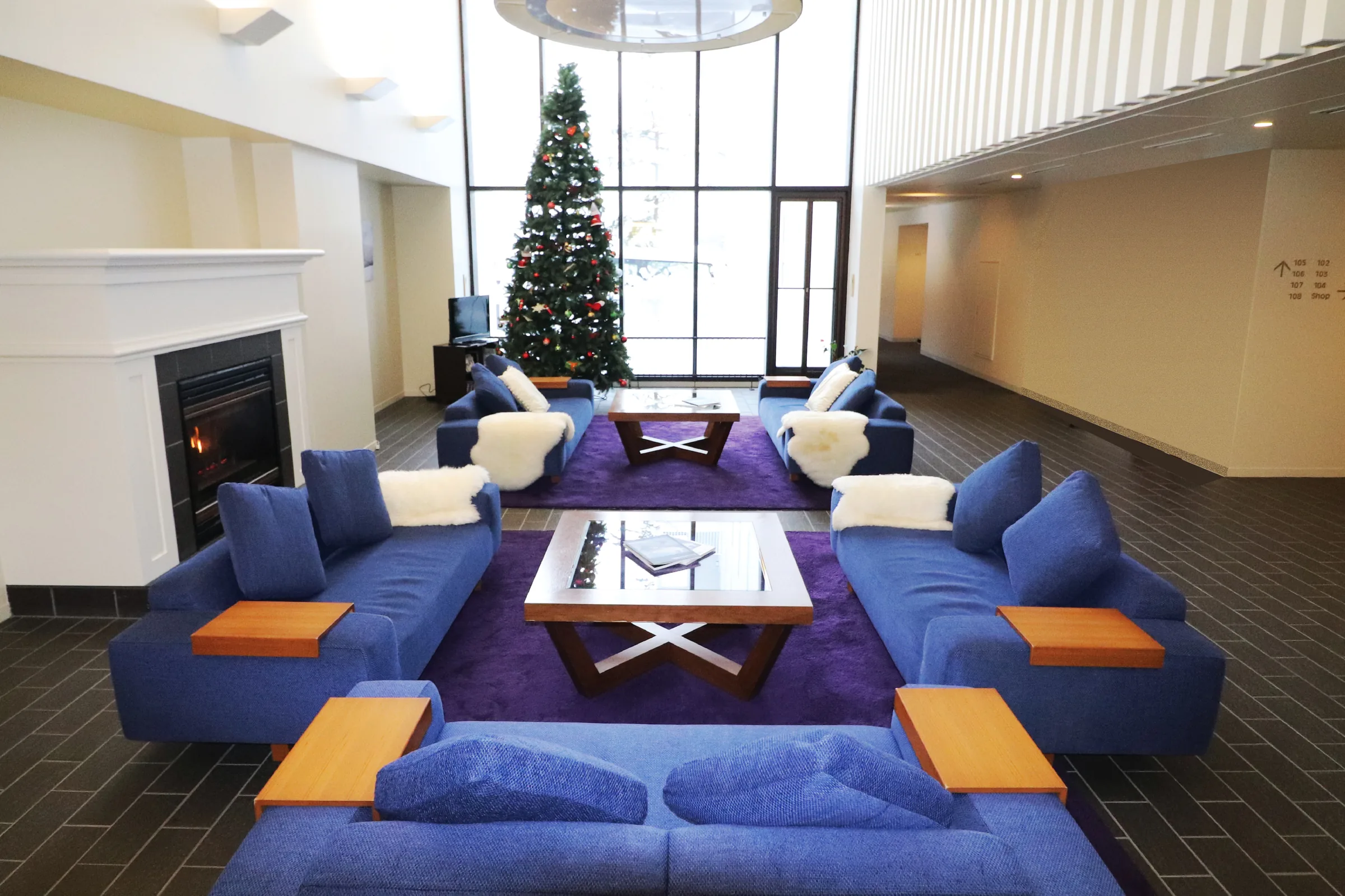 Common lounge with blue sofas, fireplace, decorated Christmas tree, and floor-to-ceiling windows.
