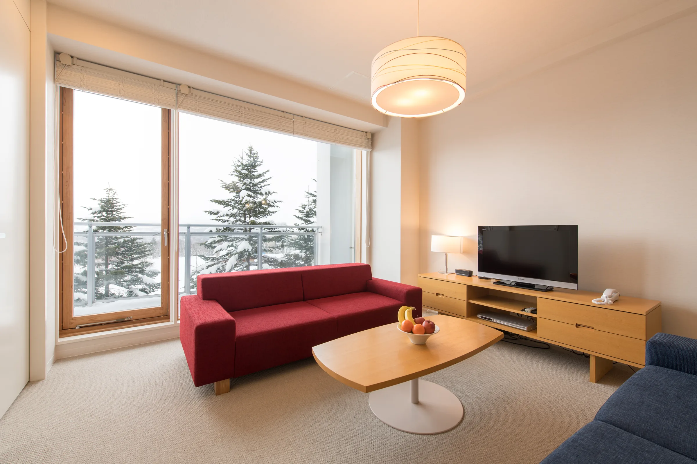 Living area with red sofa, wooden TV unit, and floor-to-ceiling windows overlooking snow-covered forest.